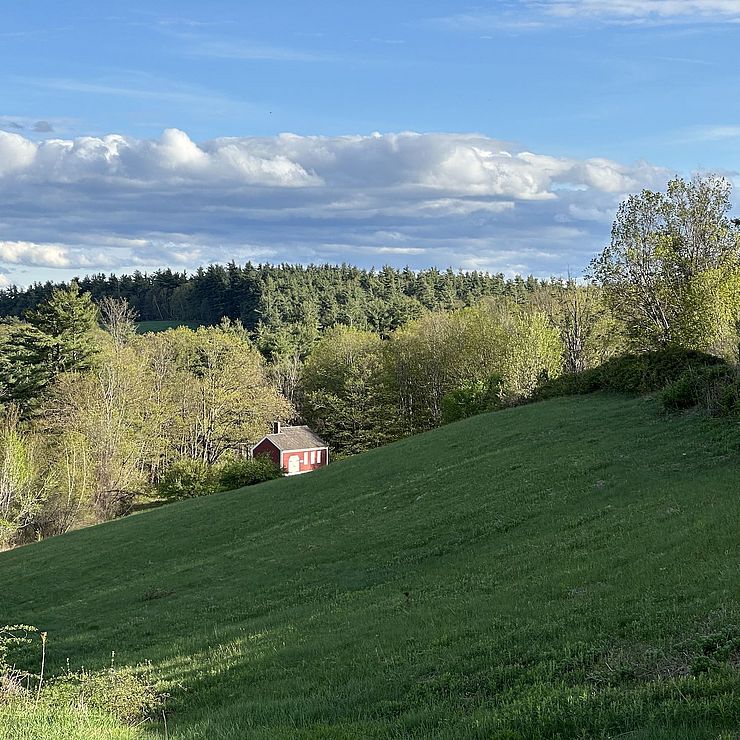 a picture of a field with a small schoolhouse in the background