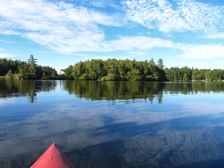 Front of red kayak on open lake with wooded island in middle